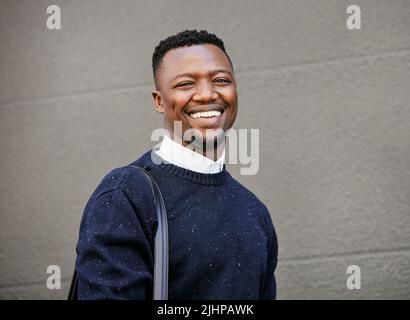 Portrait of a young businessman standing in the street in the city smiling and looking happy on a sunny day. African american male expressing Stock Photo