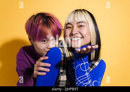 Asian couple with multicolored hair smiling while holding copyspace isolated over yellow wall Stock Photo