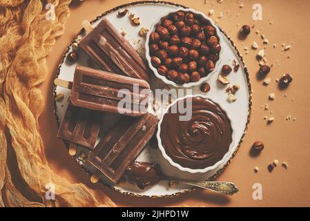 Chocolate popsicles with hazelnuts served with melted chocolate on a white plate Stock Photo