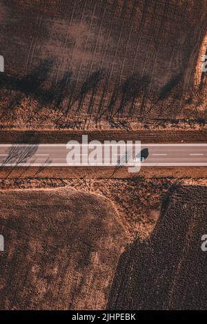 Drone shot of single gray car driving through countryside landscape in late autumn, aerial shot of miniature vehicle in travel and transport concept, Stock Photo