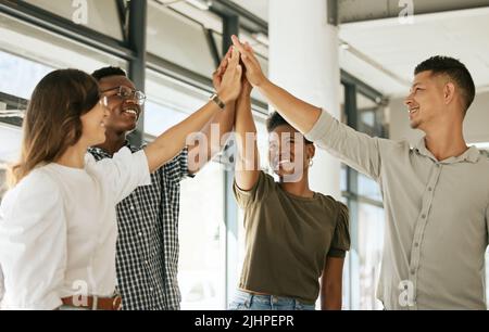 Cheerful creative business team standing in office and giving high five while celebrating a win. Diverse business people standing together at startup Stock Photo