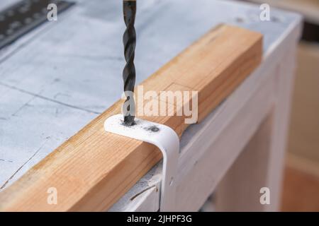 A man drills holes in an iron hook with a drill to hang a wooden screen on a battery. Stock Photo