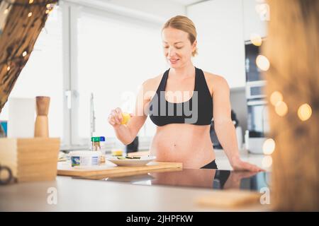 Beautiful sporty fit young pregnant woman preparing healthy meal in home kitchen. Healty lifestyle concept. Stock Photo