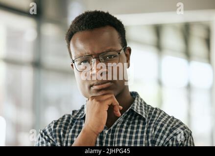 Portrait of a serious young professional african american business man with glasses and hand on chin standing in an office and looking at camera Stock Photo