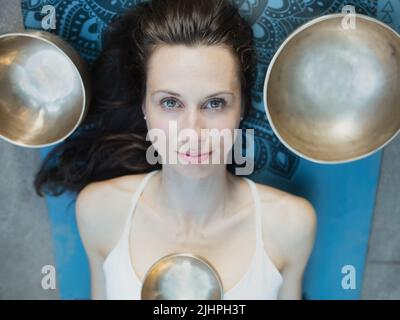Yoga concept, meditation and sound therapy. Portrait of beautiful young caucasian woman surrounded by copper tibetan singing bowls and instruments Stock Photo
