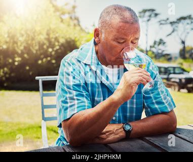 One senior mixed race man sitting alone and drinking glass of white wine during wine tasting on a vineyard. Elderly hispanic man holding and enjoying Stock Photo