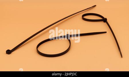 Black cable ties isolated on orange background. Plastic Tie Wraps. Stock Photo