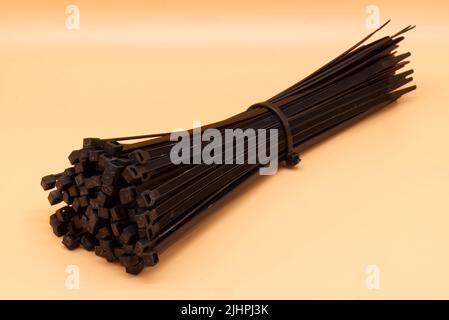 Black cable ties isolated on orange background. Plastic Tie Wraps. Stock Photo