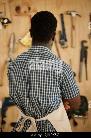 Back of african american carpenter choosing his tools. Designer standing by a wall of tools and equipment. Creative entrepreneur deciding on tools to Stock Photo