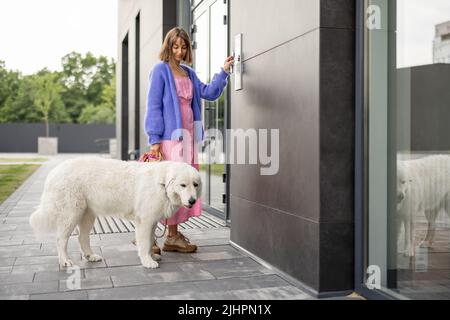 Young stylish woman getting access to the building by attaching smartphone to intercom Stock Photo