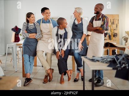 Group of five cheerful diverse clothing designers standing with their arms crossed in a shop at work. Joyful tailors smiling and laughing while Stock Photo