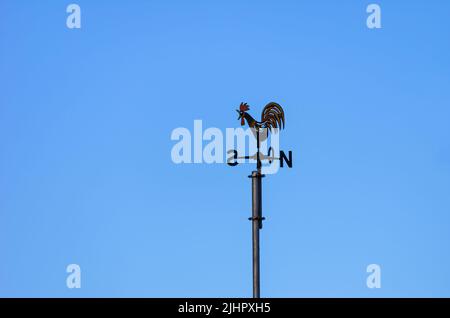 Weather vane or weathercock with wind direction indicator in the form of a compass rose on a roof against a blue sky. Stock Photo