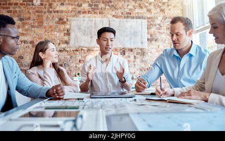 Group of diverse architects discussing plans, blueprints and schematics during a meeting in their office boardroom. Business people brainstorming and Stock Photo