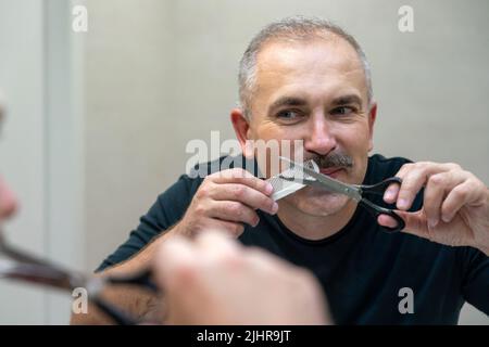Middle-aged handsome man using scissors to cut his mustache Stock Photo