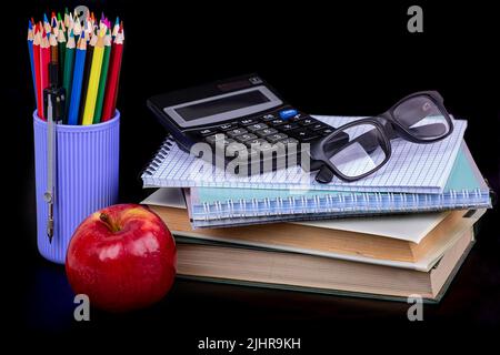 I'm going to school soon. Books, notebooks, calculator, apple, glasses and colored pencils on a black background Stock Photo