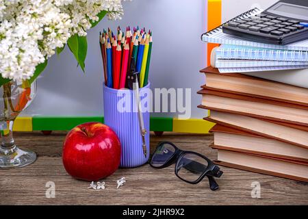 I'm going to school soon. A stack of books, notebooks, a calculator, an apple, glasses and a branch of white lilac on a wooden background Stock Photo