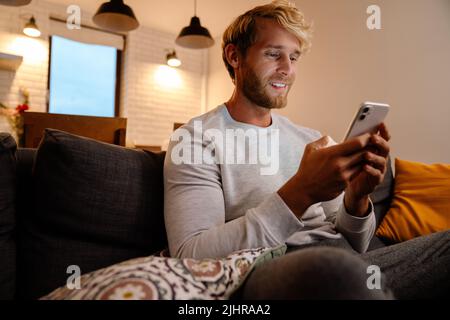 Ginger bristle man using mobile phone while sitting on sofa at home Stock Photo