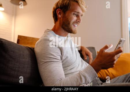 Ginger bristle man using mobile phone while sitting on sofa at home Stock Photo