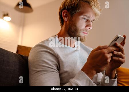 Ginger bristle man using mobile phone while sitting on sofa at home Stock Photo