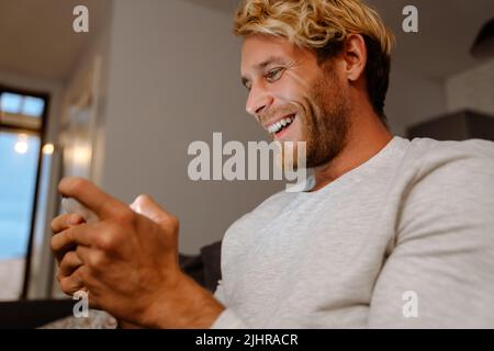 Ginger bristle man using mobile phone while sitting on sofa at home Stock Photo