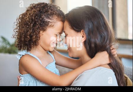 Close up of joyful mother and daughter sharing special moment while touching foreheads and sitting face to face at home. Sweet moment between parent Stock Photo