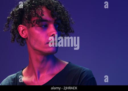 Fashionable handsome curly man in black t-shirt looks aside posing isolated on color pink blue studio background. Cool fashion offer. Virtual Reality Stock Photo