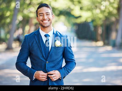 Handsome groom wearing a blue suit with a white shirt and tie. Bridegroom fastening his jacket while standing outdoors on a sunny day Stock Photo