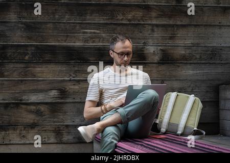 Focused man remote worker in eyewear working on laptop remotely outside. Outdoor workspace Stock Photo