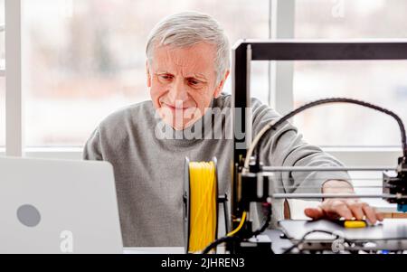 Man working on design project with laptop and 3D printer and smiling Stock Photo