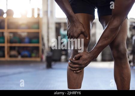 Closeup of one unknown african american athlete suffering from knee injury during workout in gym. Strong, fit, active black man feeling pain in leg Stock Photo