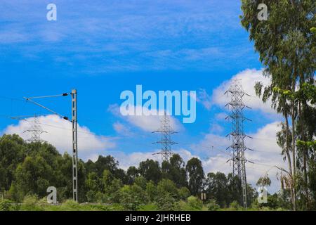 Electricity pole or electric post running through forests along with a view of electric train catenary against sky background Stock Photo