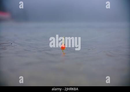 An orange and green fishing bobber floating in the water Stock