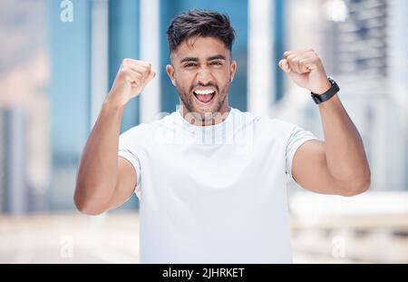 Young mixed race male athlete celebrating a goal, making a winner gesture with clenched fists after a run in the city. Cheerful fit man celebrating Stock Photo
