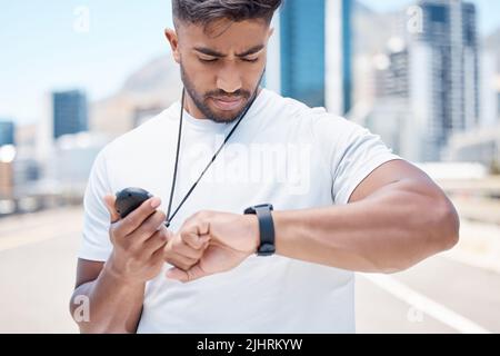 Young mixed race male athlete checking digital chronometer and smart watch to track time during a workout. Sportsman monitoring his performance or Stock Photo