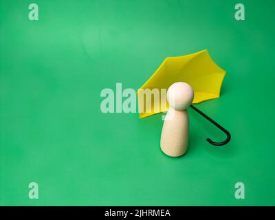 A wooden doll and umbrella on a green background a concept of insurance Stock Photo