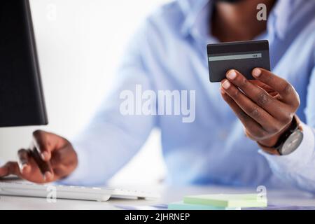 Closeup of one african american businessman spending money online with a credit card and computer in an office. Making purchase transaction with Stock Photo