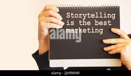 sentence Storytelling is the best Marketing, written on a black notebook in businesswoman's hands. Motivational quote. Stock Photo