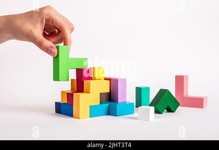 Woman hand holding puzzle element. Construction, formation, decision making, task finishing process concept. Kids wooden logical toy from multicolored bright blocks. High quality photo Stock Photo