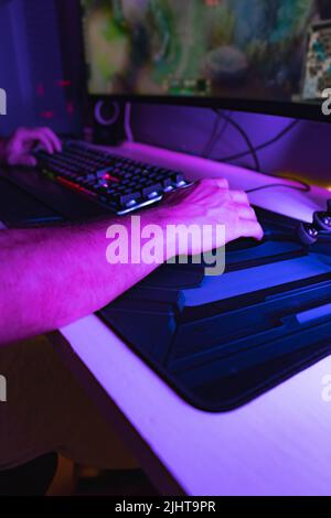 A vertical shot of hands on a mouse and keyboard playing a game on a PC in a room with blue light Stock Photo