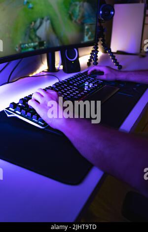 A vertical shot of hands on a mouse and keyboard playing a game on a PC in a room with blue light Stock Photo