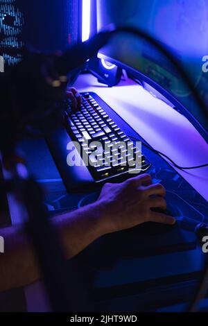 A vertical shot of hands on a mouse and keyboard playing a game on a PC in a room with blue light Stock Photo