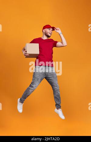 Delivery man in red cap holding cardboard box and jumping Stock Photo