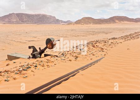 Old rusty unused railroad switch at Wadi Rum train station, tracks covered with sand near, desert and mountains in background Stock Photo