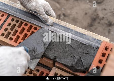 Worker or bricklayer works with trowel laying bricks. Builder makes brickwork on construction site, close up on hands. Stock Photo