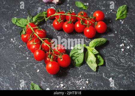 Fresh cherry tomatoes and basil with spices on a black stone background. Stock Photo