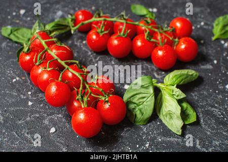 Fresh cherry tomatoes and basil with spices on a black stone background. Stock Photo