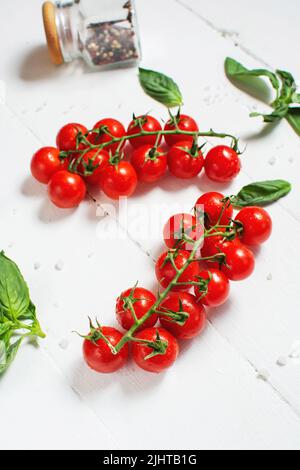 Fresh cherry tomatoes and basil with spices on a white wooden background . Stock Photo
