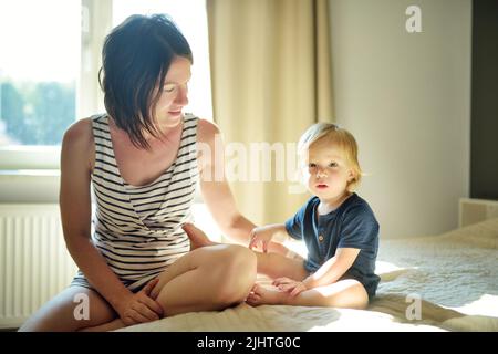 Cute funny toddler boy in his mothers arms. Mom and son having fun on sunny summer day indoors. Adorable son being held by his mommy. Stock Photo