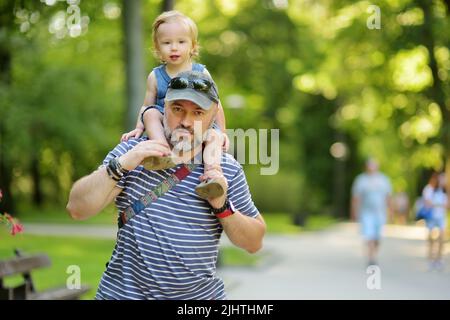 Cute toddler boy in his fathers arms. Dad and son having fun on sunny summer day in the city. Adorable baby being held by his daddy. Stock Photo