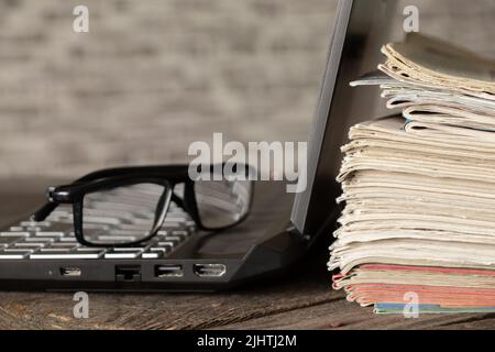 a stack of old newspapers and a laptop with glasses on a wooden table, books and computer at home, education Stock Photo
